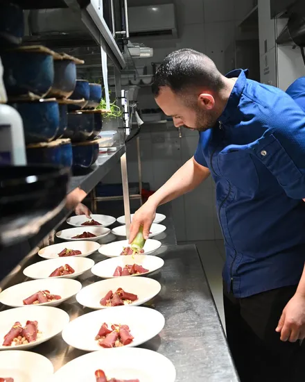 A chef in the kitchen dressing a long line of plated tuna rolls, each finished with micro herbs