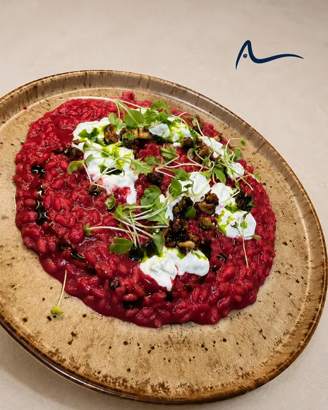 A beetroot risotto on a speckled stoneware plate with stracciatella, toasted walnuts, herb oil and micro leaves