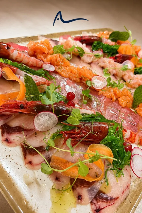 A raw seafood platter: sliced fish, red prawns, salmon, radish, samphire and herbs across a stone tray