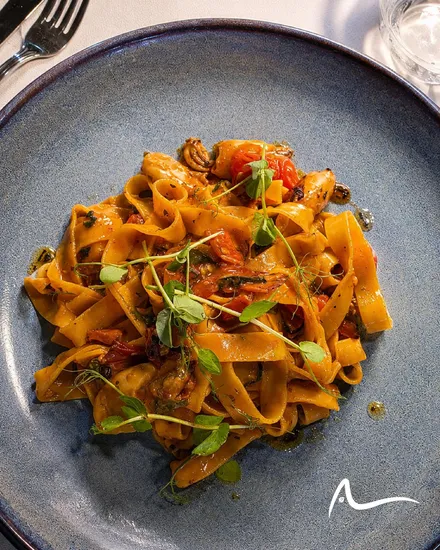 Tagliatelle with seafood in a tomato sauce, finished with pea shoots, in a blue speckled bowl