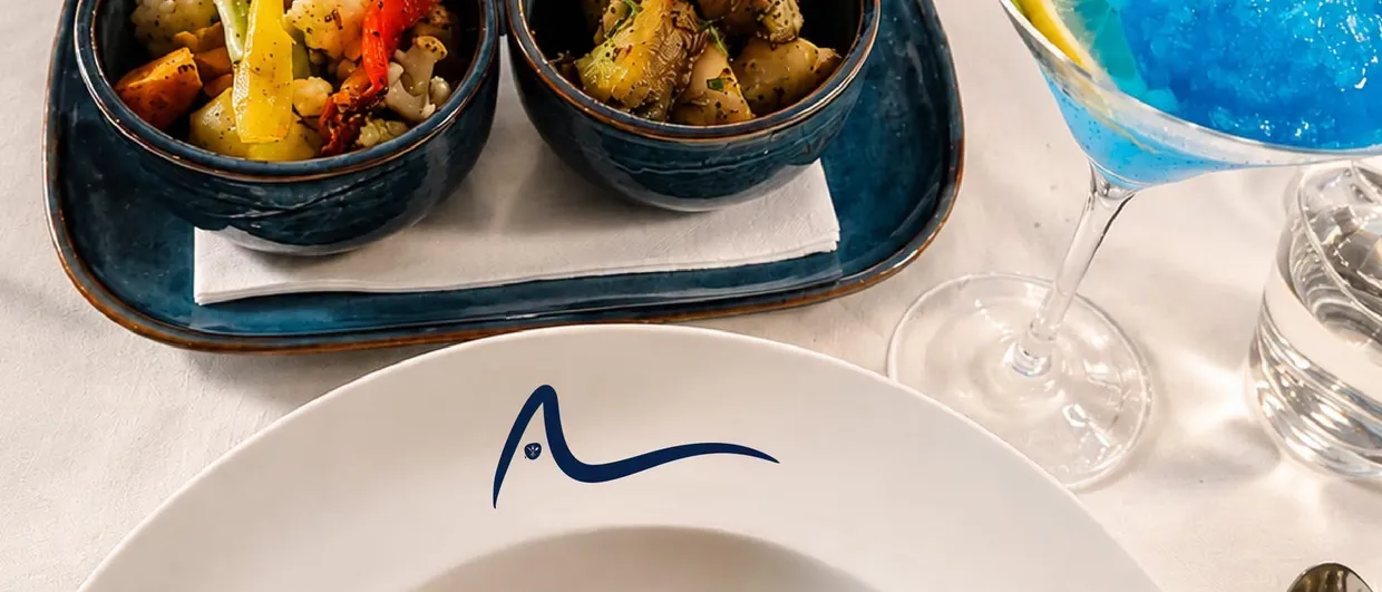 An overhead view of a laid table: grilled squid, octopus, vegetables and glasses on white linen