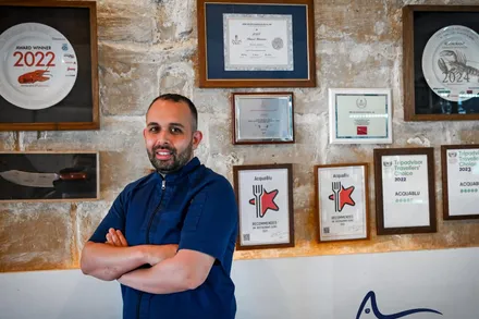 A chef standing in front of the restaurant's wall of framed certificates and award plates