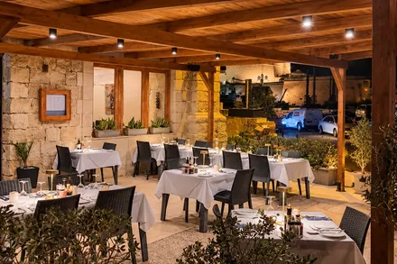 Acqua Blu's terrace after dark: tables laid with white linen under a timber pergola, lamps lit