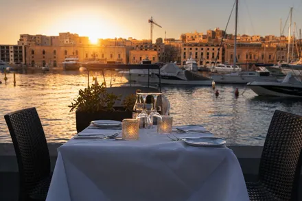 A laid table at the water’s edge at sunset with boats behind